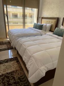 2 große Betten in einem Zimmer mit einem großen Fenster in der Unterkunft Marina Saidia Luxury Apartment with pool & Garden view. Residence Tamaris in Saidia 