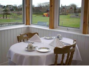 a table with a white tablecloth and two chairs and two windows at Glenshee Guest House in Golspie