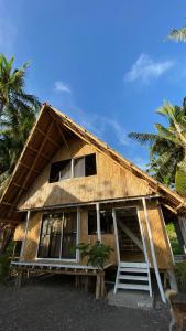 a house with a thatched roof and palm trees at Villa Eliza Ecofarm in Tibiao