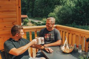 two men sitting at a table on a deck at Frankenwald Chalets - Chalets in Wilhelmsthal