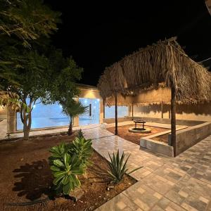 a resort at night with a table and a straw umbrella at استراحة وشاليه الكوخ in Unayzah