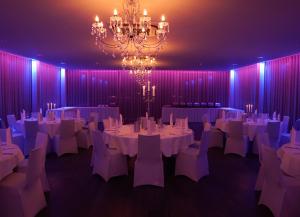 Cette grande chambre comprend des tables et des chaises blanches ainsi qu'un lustre. dans l'établissement Hotel Sportforum, à Rostock