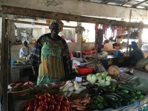 a woman standing next to a table of vegetables at La Mangrove Villa paisible dans un cadre luxuriant in Cap Skirring