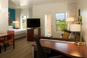 Habitación de hotel con escritorio y dormitorio con cama y TV. en Residence Inn Palm Desert en Palm Desert
