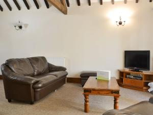 a living room with a leather couch and a tv at Littlewood Barn - Ukc3737 in Bawdeswell