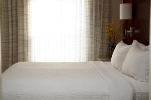 a bed with white sheets and pillows in front of a window at Residence Inn Appleton in Appleton