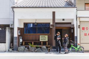 due persone in piedi di fronte a un palazzo con una bicicletta di Couch Potato Hostel - Vacation STAY 88241 a Matsumoto