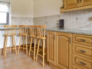 a kitchen with wooden cabinets and bar stools at Baileys Barn - Ukc3738 in Bawdeswell