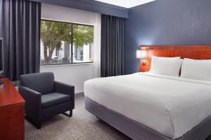 um quarto com uma cama, uma cadeira e uma janela em Courtyard by Marriott Raleigh Midtown em Raleigh