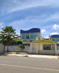 a building with a white fence and a palm tree at Pousada Aruamar in Aracaju