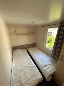 two beds in a small room with a window at MobilHome 3 chambres 6 personnes Piscine Camping Saint Cheron in Saint-Chéron