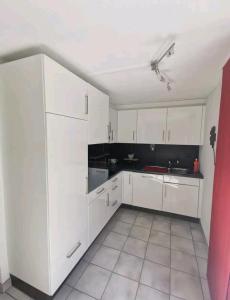 a white kitchen with white cabinets and a red wall at Studio à Courrendlin in Courrendlin