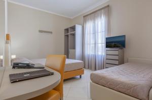 a room with two beds and a desk with a laptop at Ghibli Hotel in San Vito lo Capo