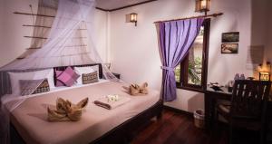 a bedroom with a bed with purple curtains and a window at Baan Manali Resort in Thongsala