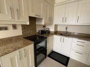 a white kitchen with white cabinets and black appliances at Apartment at Island Cottage, Inishnee, Roundstone in Galway