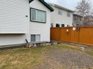 a white house with a wooden fence and a patio at Super Luxury & Cozy Lower Level Apartment in NW Calgary, AB Close to Banff in Calgary