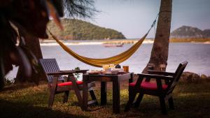 a table and two chairs and a hammock by the water at Baan Manali Resort in Thongsala