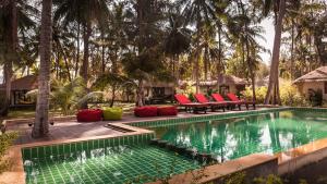 a swimming pool with red chairs and palm trees at Baan Manali Resort in Thongsala