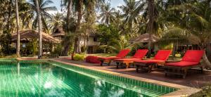 a swimming pool with red chairs next to a resort at Baan Manali Resort in Thongsala