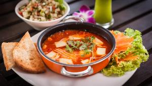 a bowl of soup on a plate with bread and salad at Baan Manali Resort in Thongsala