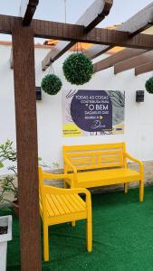 dois bancos amarelos sentados ao lado de uma parede com uma placa em Studios Unamar em Cabo Frio