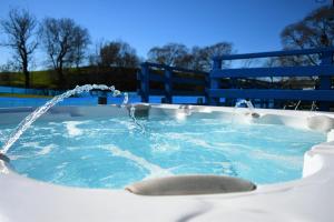 uma banheira de hidromassagem com duas fontes e um banco azul em Glen Roe - 3 Bed Lodge on Friendly Farm Stay with Private Hot Tub em New Cumnock