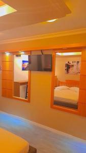 1 dormitorio con TV, cama y espejo en Motel Avenida (Adult Only), en Gramado