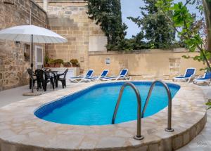 a pool with chairs and a table and an umbrella at Il Gnejna in Xagħra