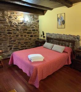 1 dormitorio con cama roja y pared de piedra en Casa Freixe Apartamentos Rurales, en Santa Eulalia de Oscos