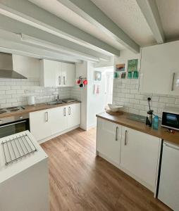 a large kitchen with white cabinets and wooden floors at SEREN cottage by the sea in Llangadwaladr