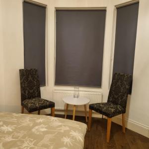 a bedroom with two chairs and a table and two windows at 41 Crawley Road in Luton