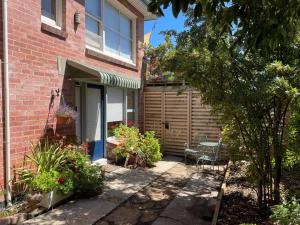 uma casa de tijolos com um alpendre com um banco e flores em The Undercroft - Cosy boutique studio apartment. em Moonah