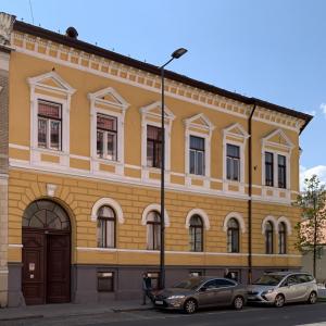 un bâtiment jaune avec deux voitures garées devant lui dans l'établissement Charming Central Apartments, à Cluj-Napoca