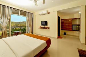 Schlafzimmer mit einem Bett, einem TV und einem Balkon in der Unterkunft Hotel Sadhana Executive in Dapoli