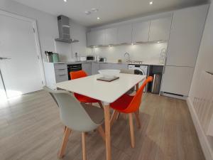 a kitchen with a white table and orange chairs at 8 Putsborough - Luxury Apartment at Byron Woolacombe, only 4 minute walk to Woolacombe Beach! in Woolacombe