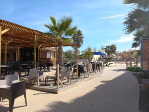 eine Terrasse mit Tischen, Stühlen und Palmen in der Unterkunft Mobil-home Les Locs Danous in Valras-Plage