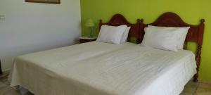 Cette chambre comprend un lit avec des draps blancs et un mur vert. dans l'établissement Vivenda Familia Pedro, à Vila do Bispo