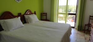a bedroom with a bed with white sheets and a window at Vivenda Familia Pedro in Vila do Bispo