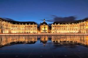 a large building with its reflection in the water at night at Appartement Bordeaux meublé tourisme classé 3 étoiles in Bruges