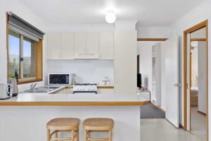 a white kitchen with two stools and a counter at Grovedale Home Away From Home in Grovedale