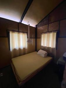 ein kleines Bett in einem Zimmer mit zwei Fenstern in der Unterkunft Auntie Mina's Beach Cabins in Puerto Princesa