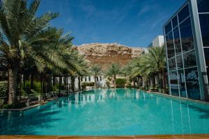 a large swimming pool with palm trees in front of a building at Alberni Jabal Hafeet Hotel Al Ain in Al Ain