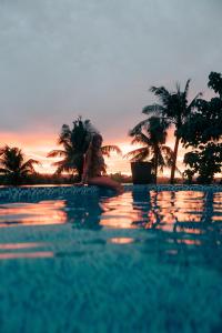 a woman sitting on the edge of a swimming pool at sunset at Lexias Hostel and Workspace - Siargao in Catagnan
