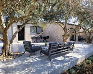 a patio with two benches and a table and trees at Villa Grioni, beach front villa with jacuzzi in Novalja