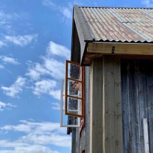 eine Person, die aus einem Fenster eines Hauses blickt in der Unterkunft Husmannsplassen Havrebakken på Helgøya in Ringsaker