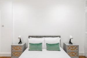 uma cama branca com duas mesas de cabeceira e duas almofadas verdes em Hububb Luxury Knightsbridge House em Londres