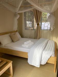 um quarto com uma cama com lençóis brancos e uma janela em Golden Cherries Guest House em Jinja