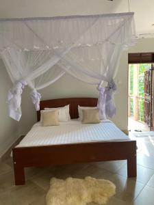 a bed with a canopy with white curtains and a rug at Golden Cherries Guest House in Jinja