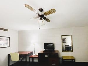 een kamer met een plafondventilator en een bureau met een televisie bij The Madison Inn Motel in Fort Madison
