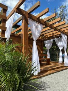 a wooden pergola with white curtains on a patio at Pousada Maria Eduarda in Guarda do Embaú